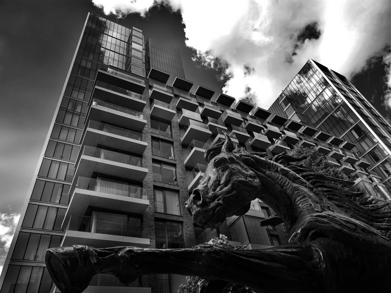 Black and white photo of a skyscraper with a dynamic horse sculpture in the foreground, dramatic urban scene.